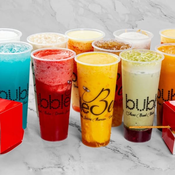 Assortment of colorful bubble teas and fruit juices in clear plastic cups on a marble surface.