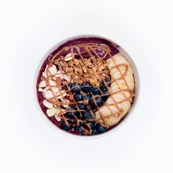 Overhead view of an acai bowl with blueberries, banana slices, granola, almonds, and peanut butter drizzle.