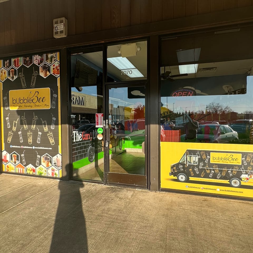 Exterior of BubbleBee bubble tea shop with large window decals featuring drinks and a food truck.