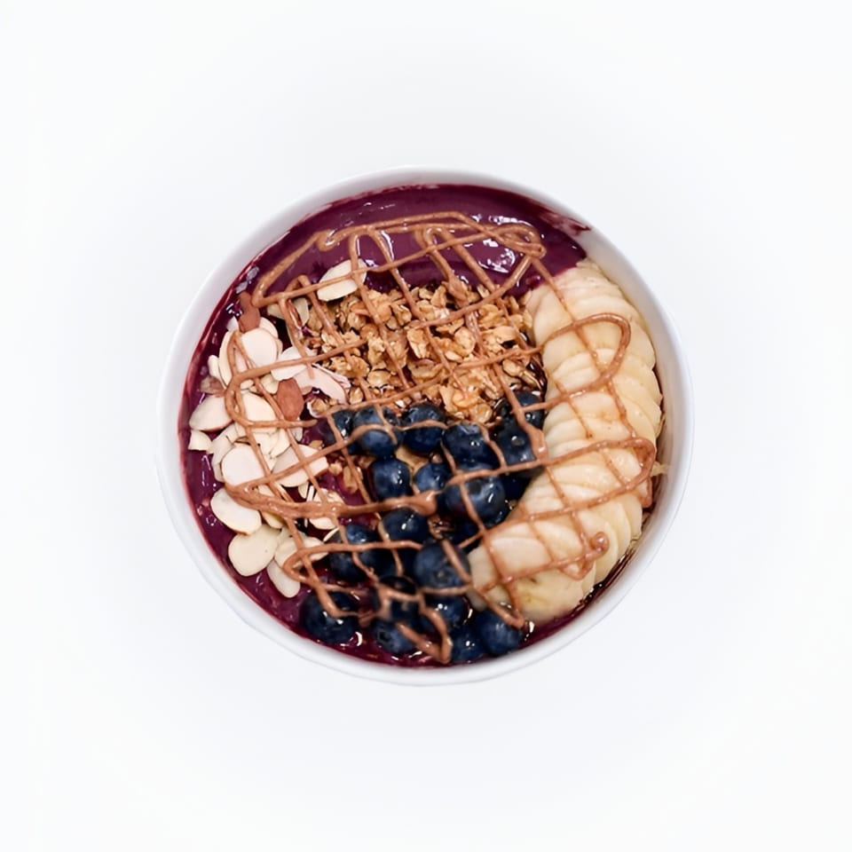 Overhead view of an acai bowl with blueberries, banana slices, granola, almonds, and peanut butter drizzle.