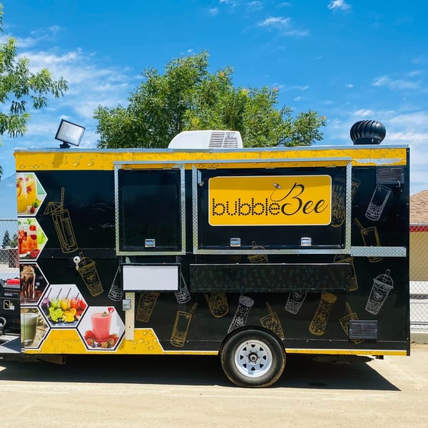 Black and yellow Bubble Bee food truck with drink images and logo under a blue sky.