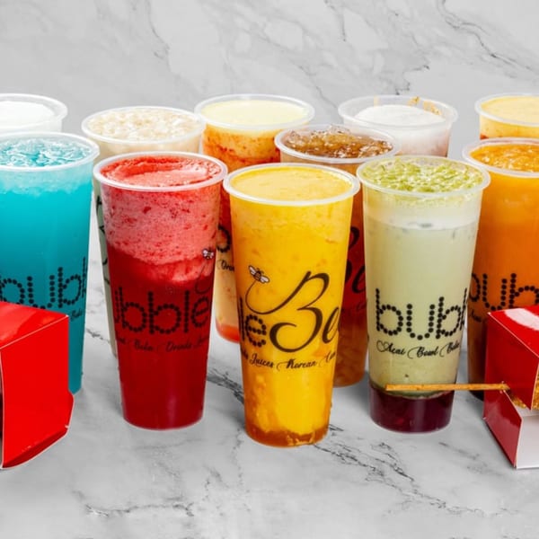 A vibrant assortment of colorful bubble teas and juices in clear plastic cups on a marble surface.