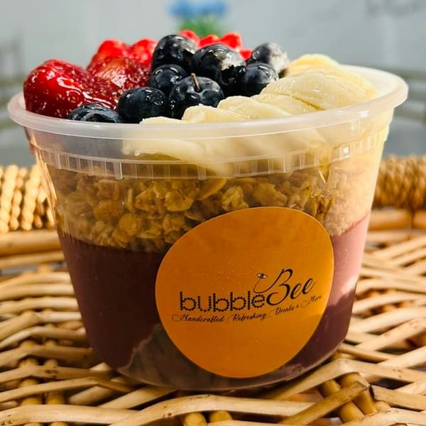 Bubble Bee açaí bowl with strawberries, blueberries, bananas, and granola on a woven mat.