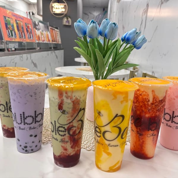 Six colorful boba tea drinks with various fruit toppings and flavors on a white counter.