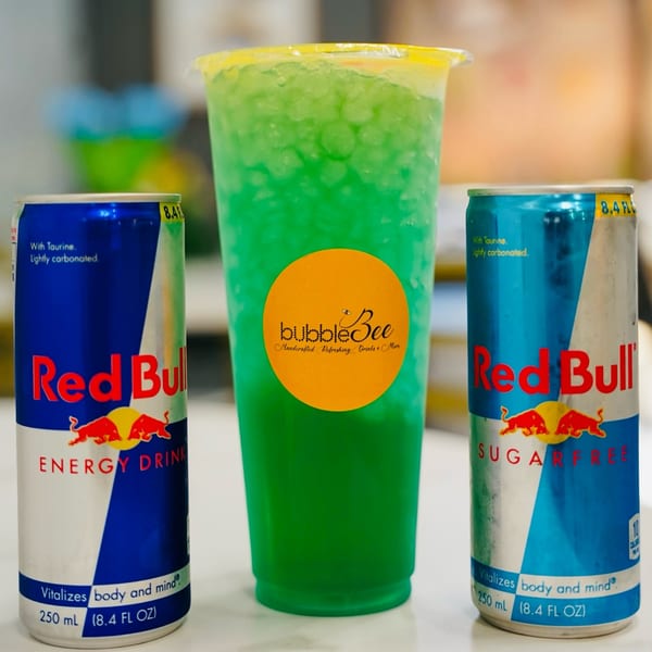 Bubble Bee green drink with two Red Bull cans on a white surface.