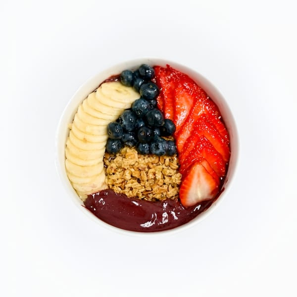 A vibrant acai bowl with bananas, blueberries, strawberries, and granola on a white background.
