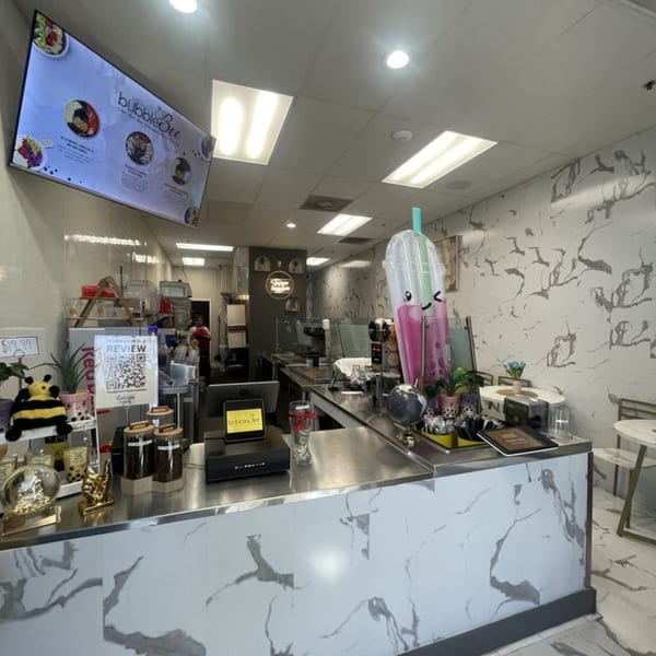 Interior of BubbleBee, a bubble tea shop, with a menu screen, counter, and seating.