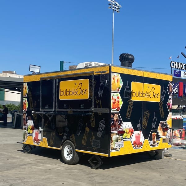 A black and yellow Bubble Bee food truck with drink images parked on asphalt under a clear sky.