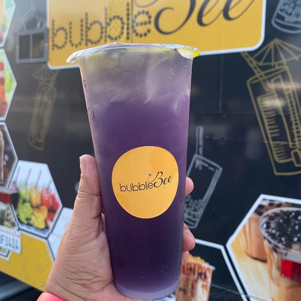 Hand holding a purple Bubble Bee drink with ice, against a black and yellow background.
