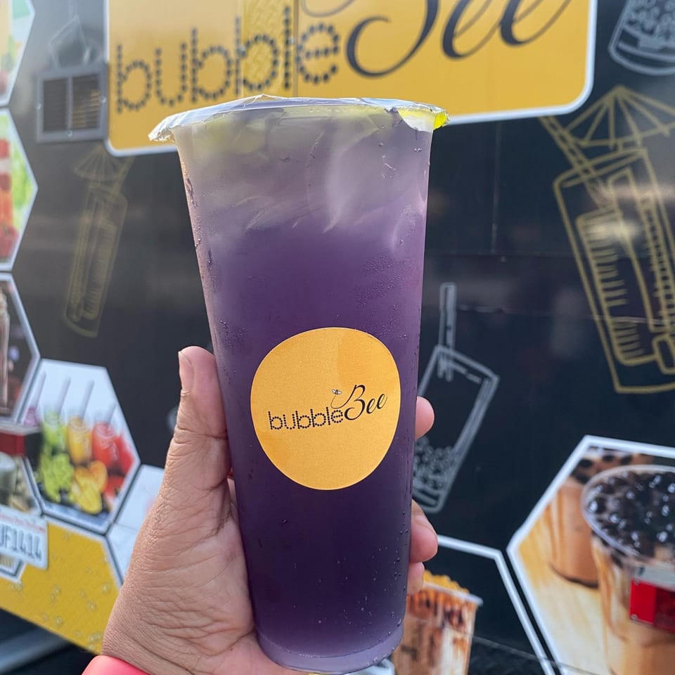 Hand holding a purple Bubble Bee drink with ice, against a black and yellow background.